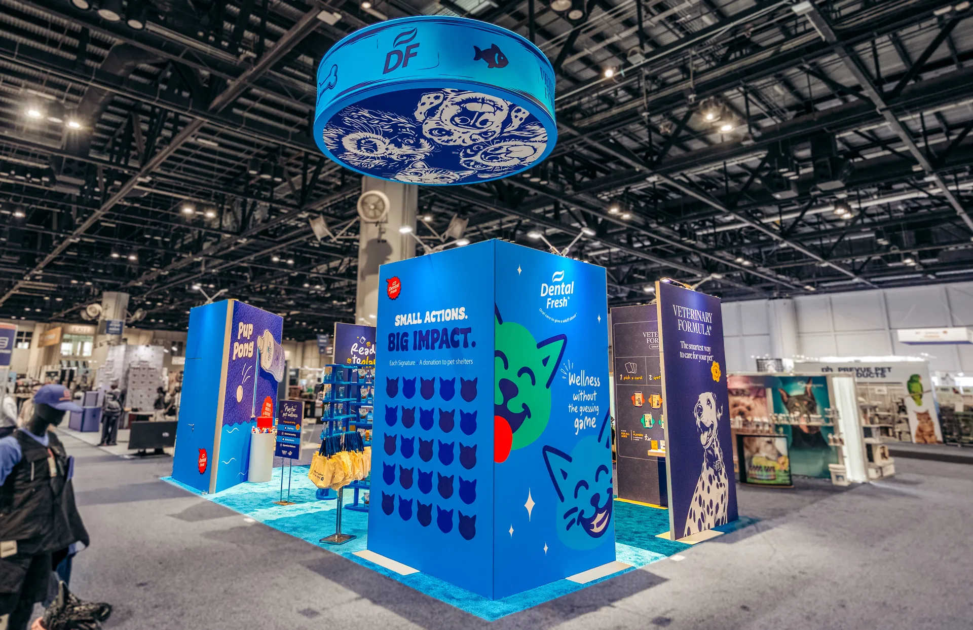 Synergy Labs island exhibit with a suspended drum sign and branded towers