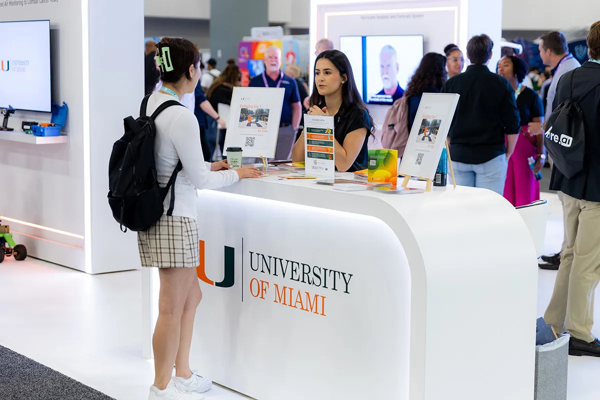Students talking with University of Miami staff at a branded kiosk