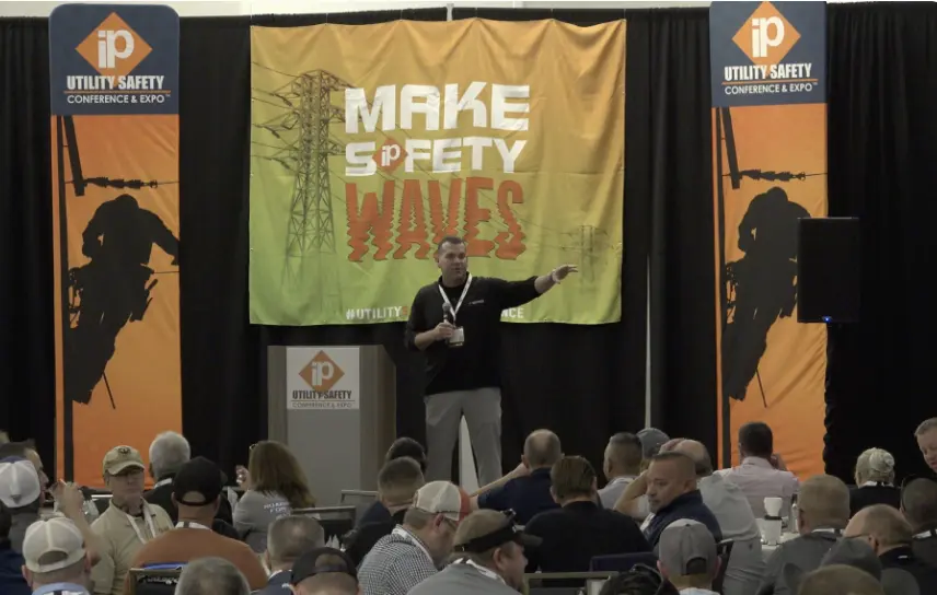 A speaker presents to an audience in front of a banner that reads "Make Safety Waves" at the iP Utility Safety Conference & Expo.